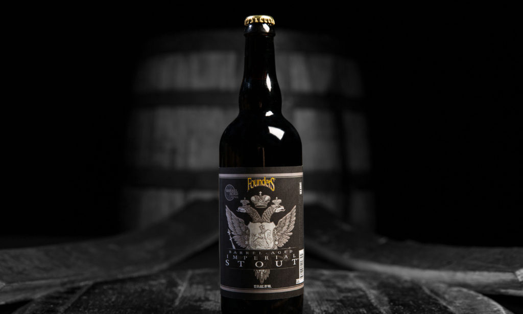 black and white barrel-aged imperial stout bottle positioned on bourbon barrels