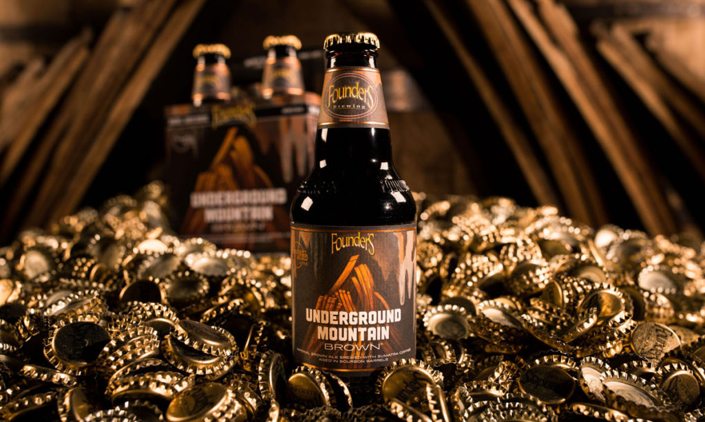 Underground Mountain Brown bottle in front of 4-pack among gold bottle caps