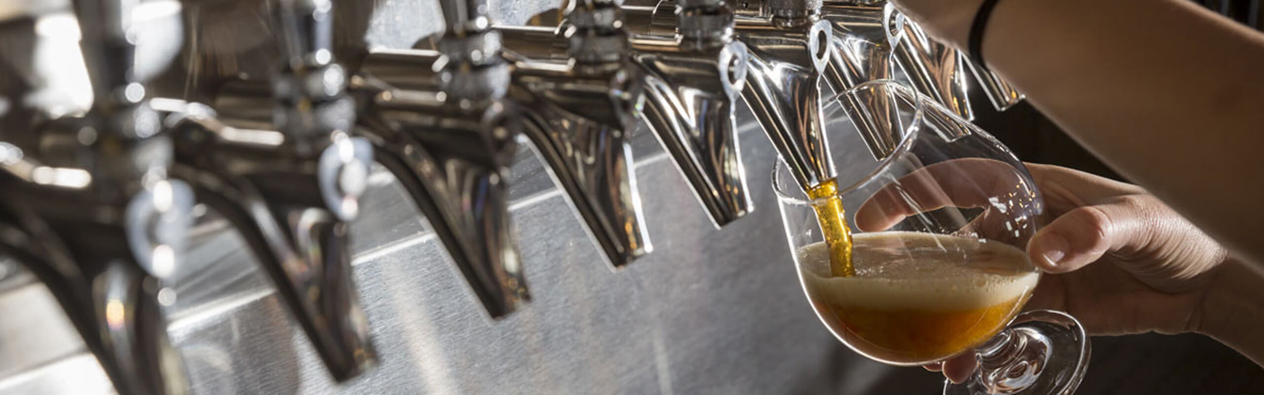Row of tap handles and taps with one pouring beer into a snifter glass