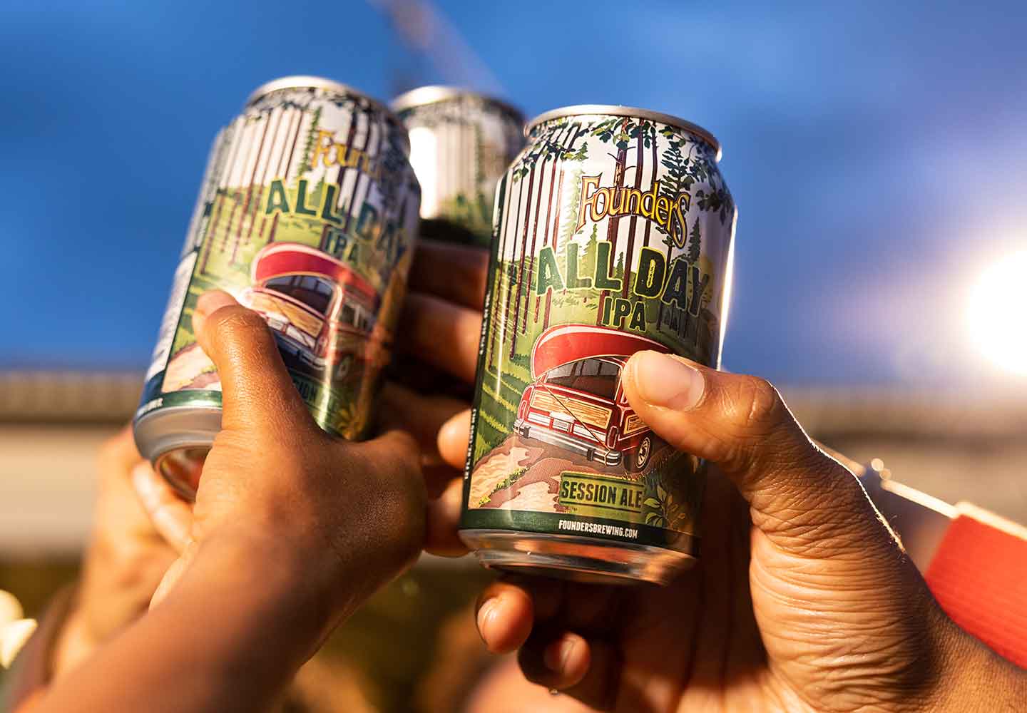 Cans of All Day IPA being raised together by hands