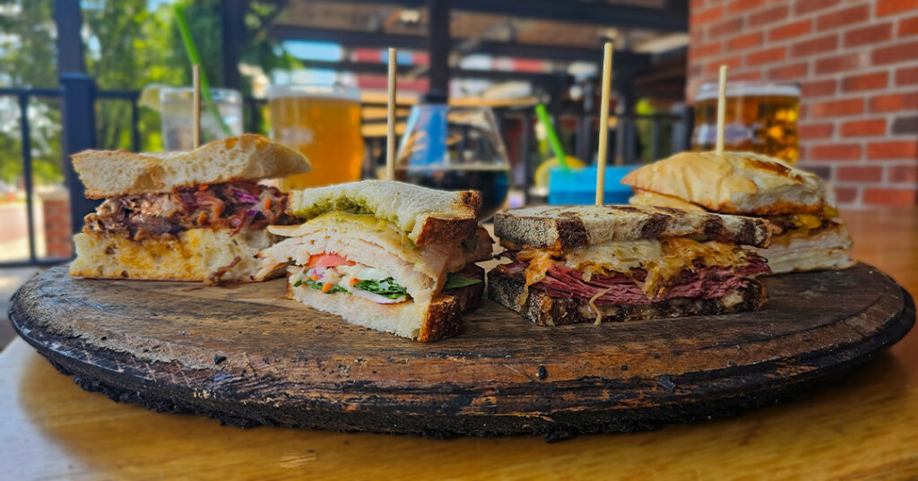 sandwiches on a platter in front of a variety of beverages on a porch