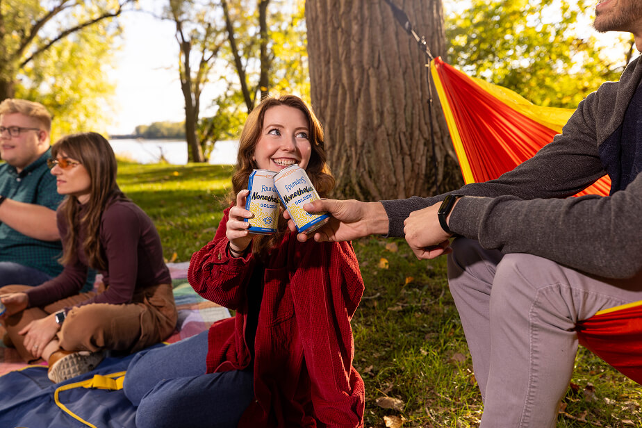 People sitting on the ground smiling with Nonetheless beer cans in hand